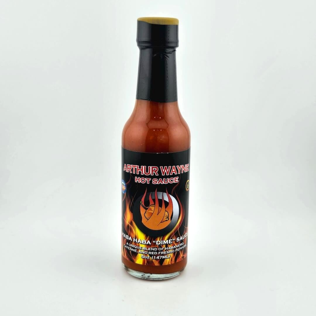 Glass bottle of hot sauce safety sealed with plastic. Label across main body of bottle details flavor and image depicting it.