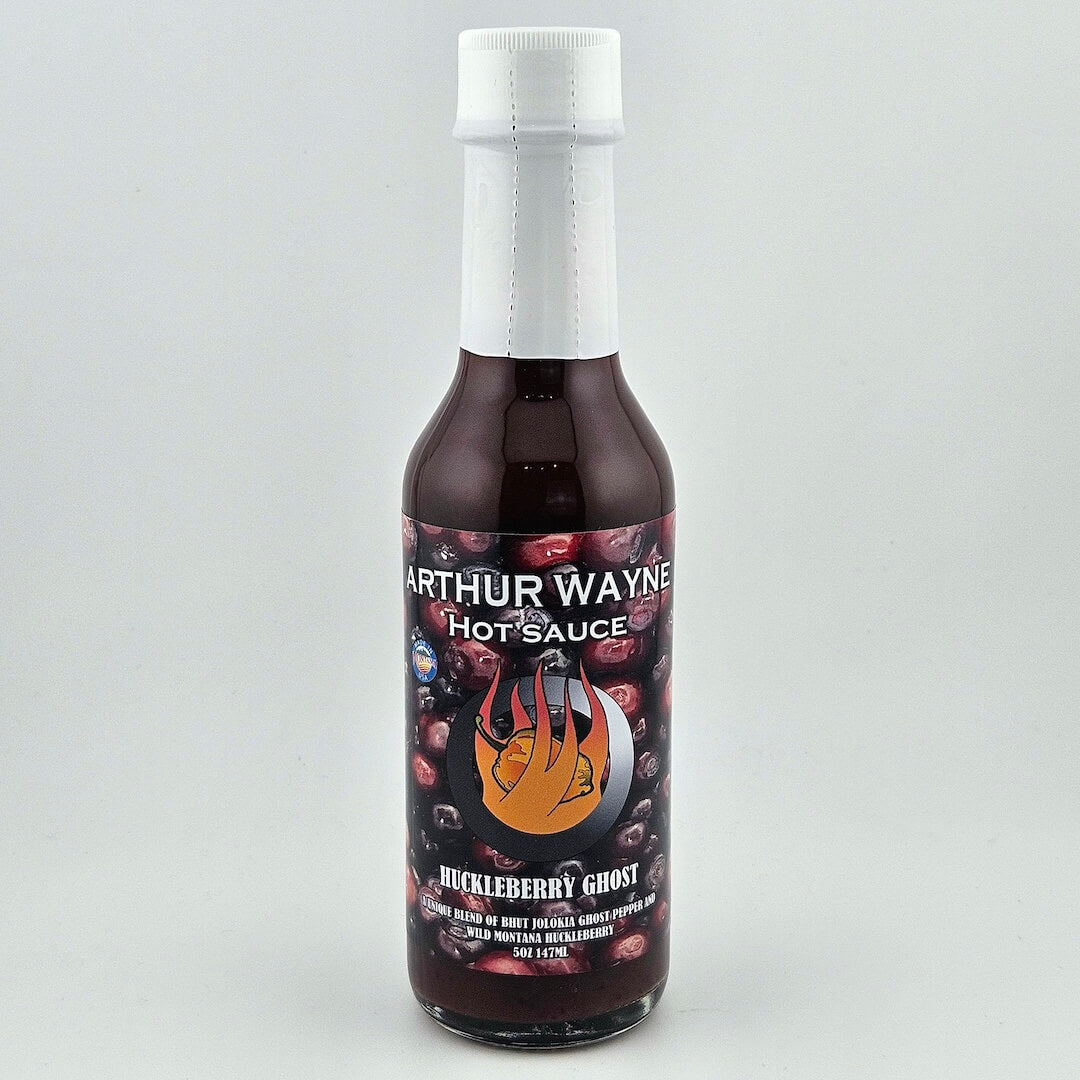 Glass bottle sealed with white plastic. Label has huckleberries pictured behind flaming pepper image in center.