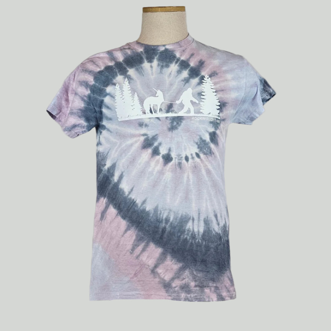 Lavender & navy tie Dye shirt with silhouette of trees either side of Bigfoot leading a unicorn on a leash.