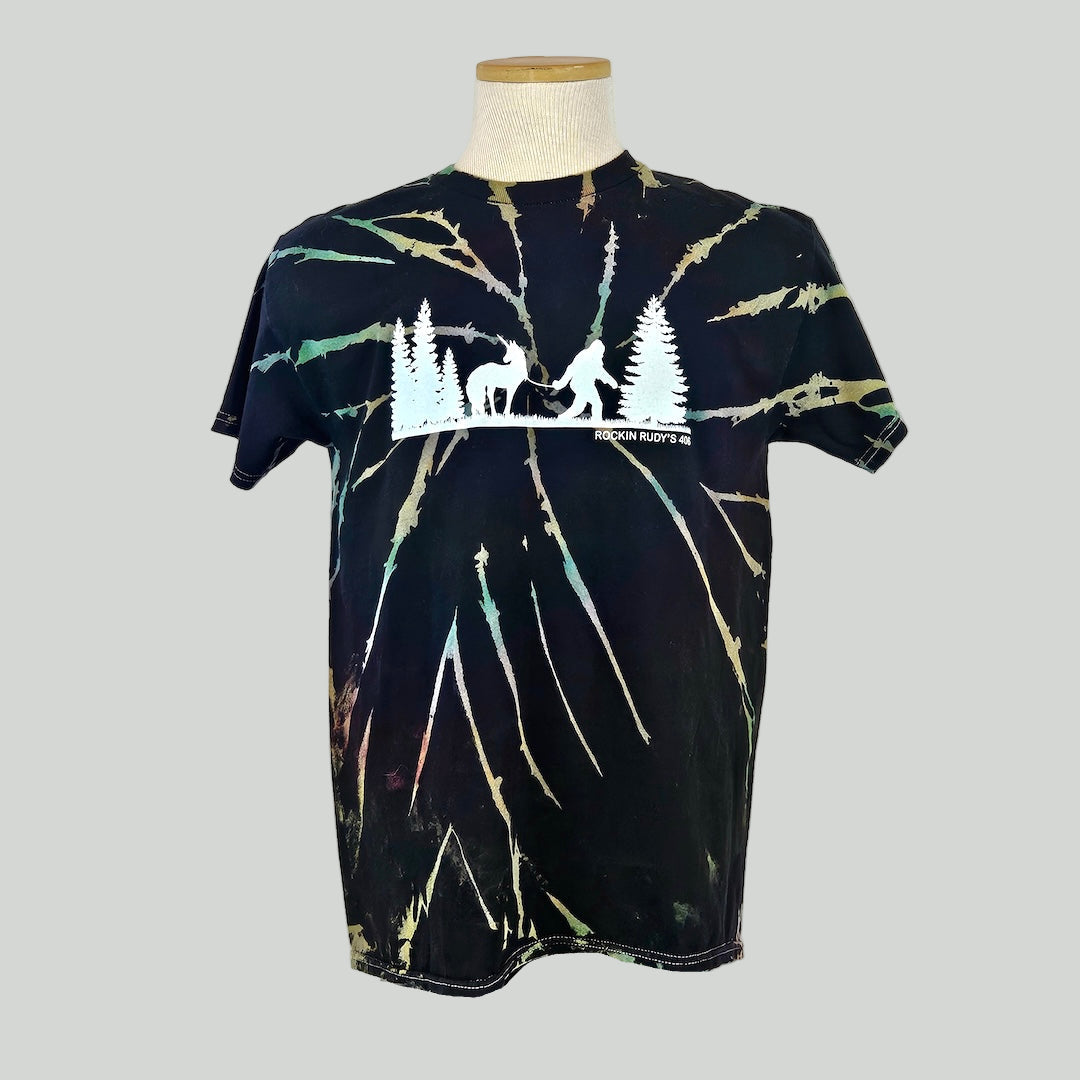 Black tie Dye shirt with silhouette of trees either side of Bigfoot leading a unicorn on a leash.