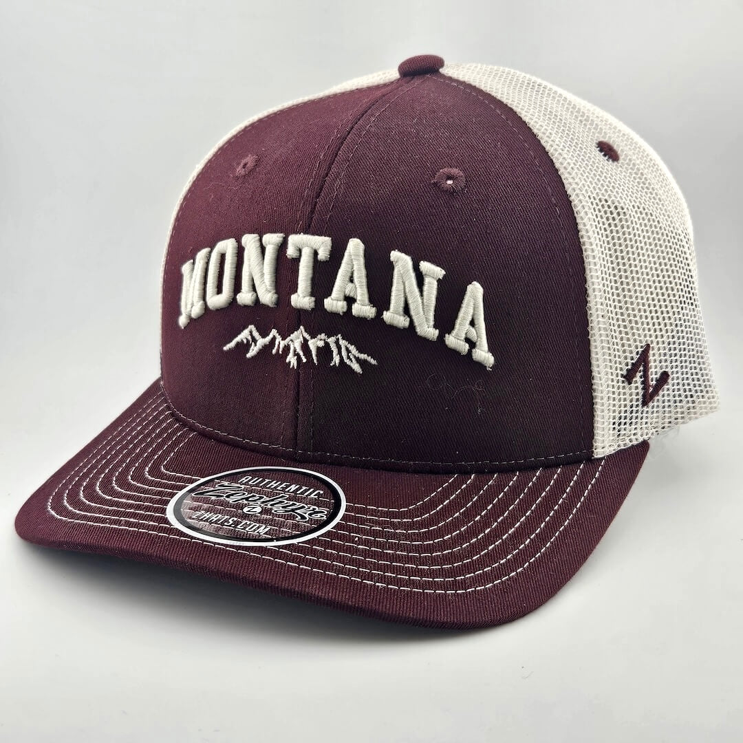 Maroon face & billed hat, white mesh back & stitching. "MONTANA" embroidered able mountain range silhouette. Sticker on brim.
