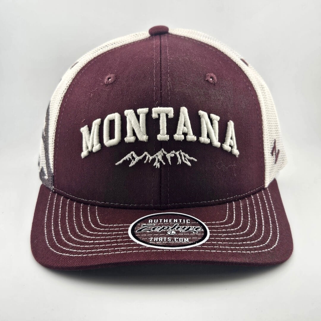 Maroon face & billed hat, white mesh back & stitching. "MONTANA" embroidered able mountain range silhouette. Sticker on brim.