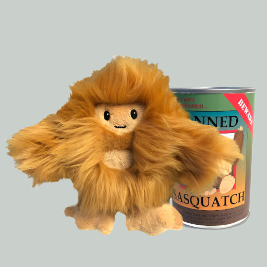 Plush toy resembling a creature with a can labeled 'Canned Sasquatch' on a gray background