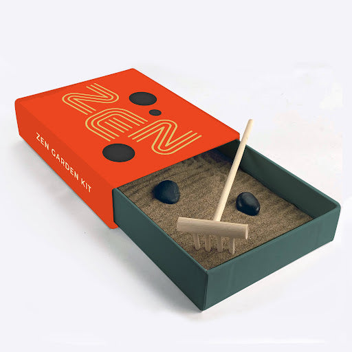 Zen garden kit opened to show stones among sand bed with small wooden rake.
