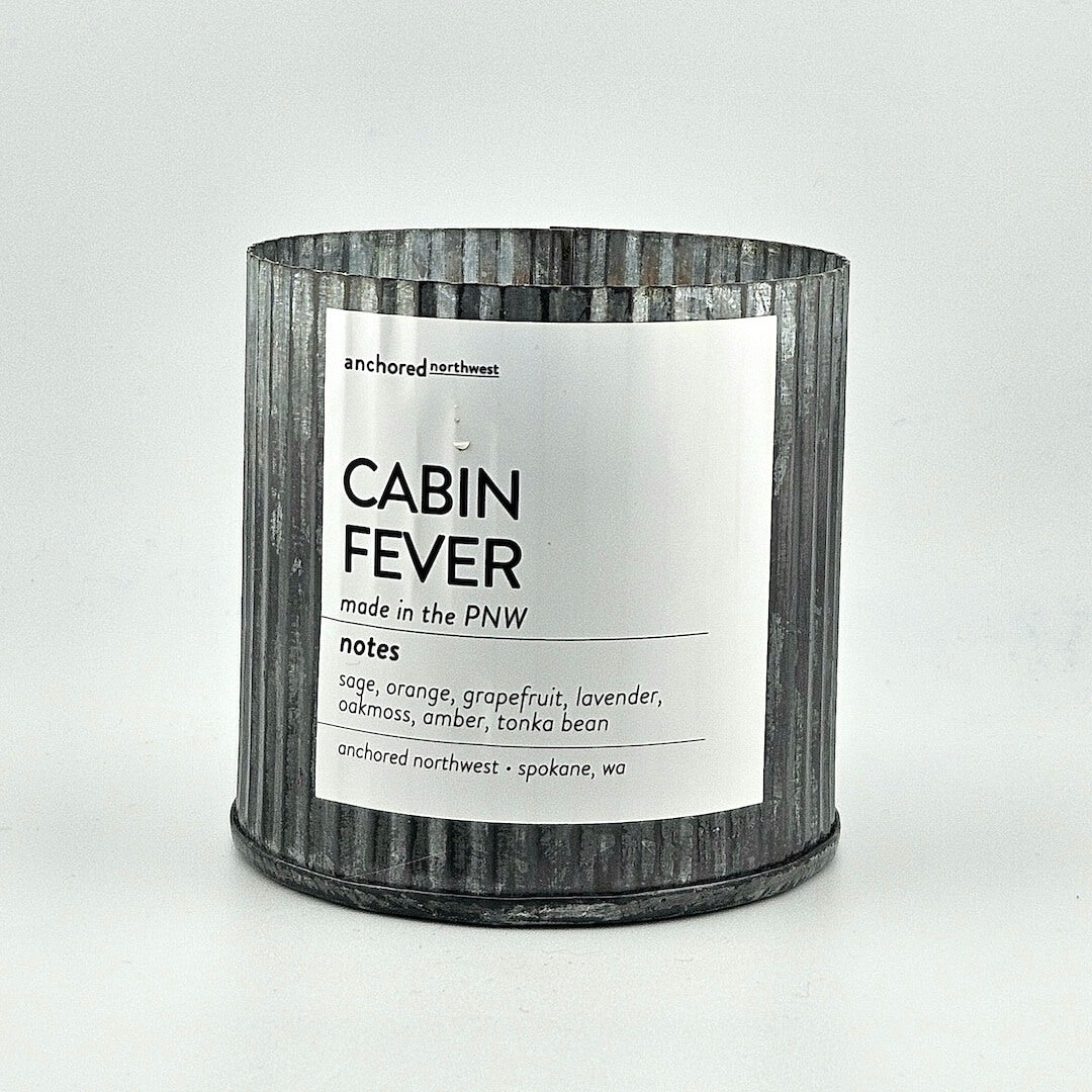 Candle labeled 'Cabin Fever' with a metal-textured container on a white background