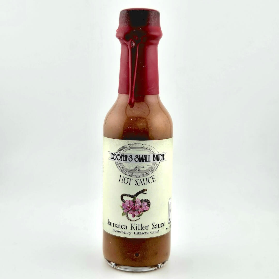 Bottle of Jamaica Killer Sauce with a red cap on a white background