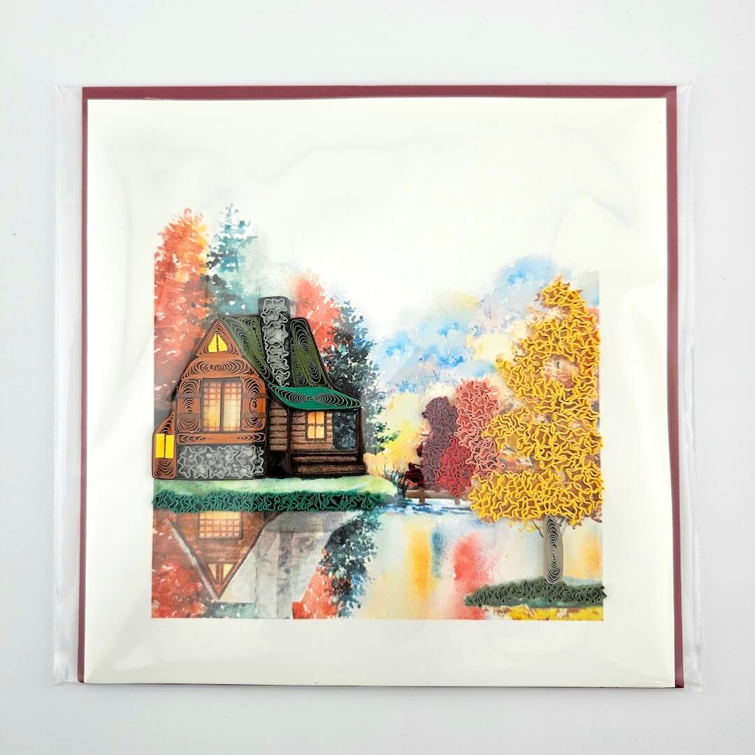 Quilled artwork of a cozy cabin in the woods with colorful trees and a person walking.