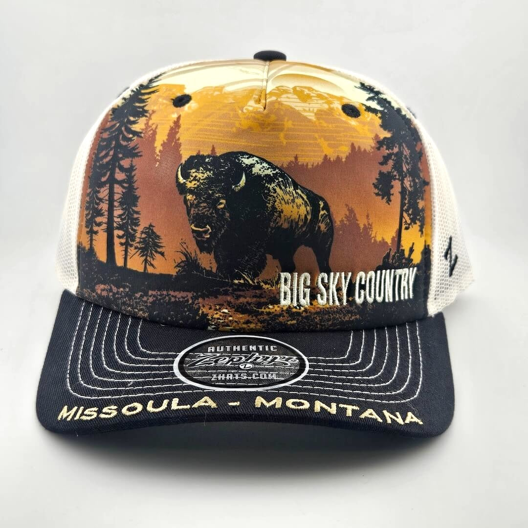 Trucker hat with mountain landscape across face with bison as central image. Missoula, Montana embroidered across bill.