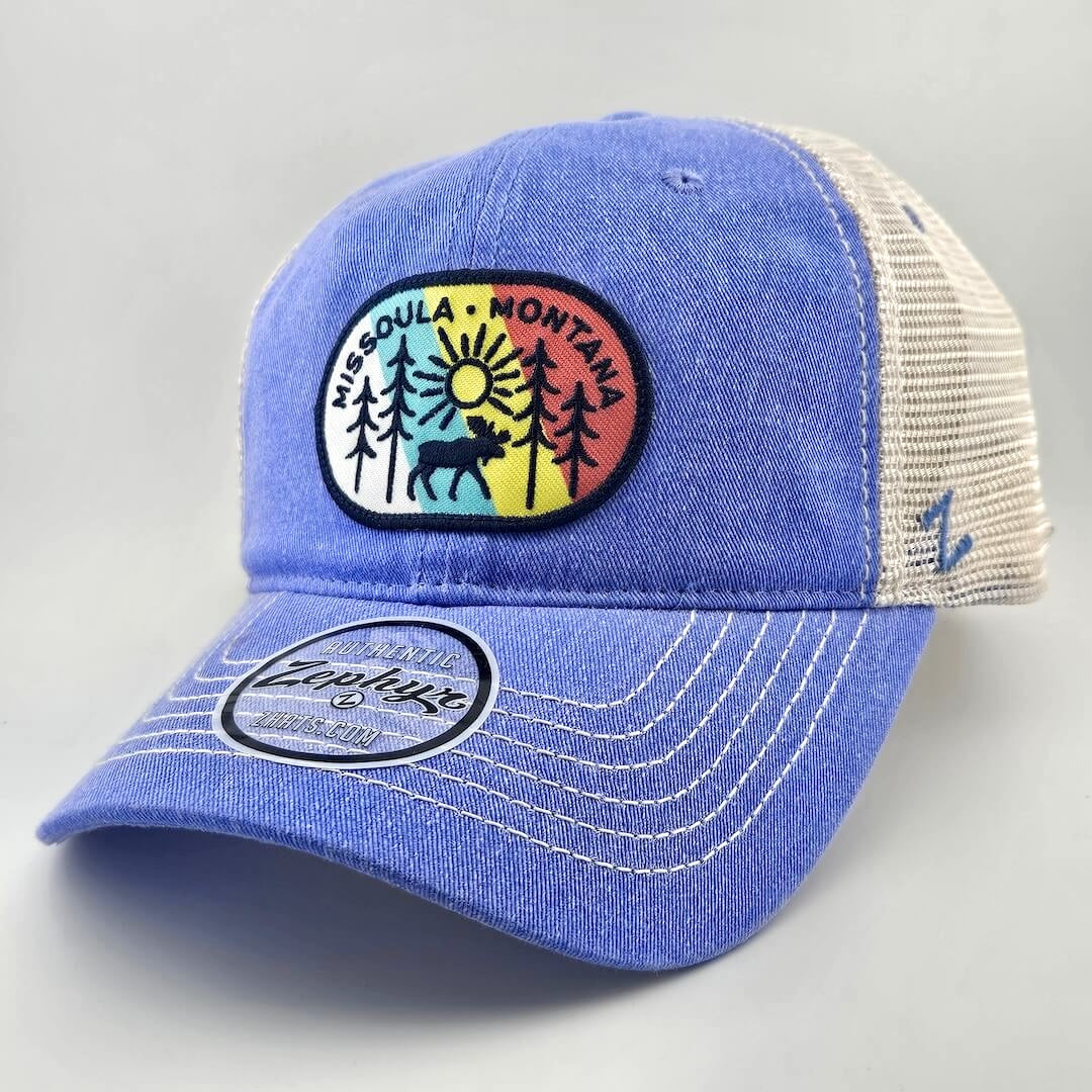 Blue ball cap with white mesh back & stitching, multicolored patch on face with tree line drawing & city name.