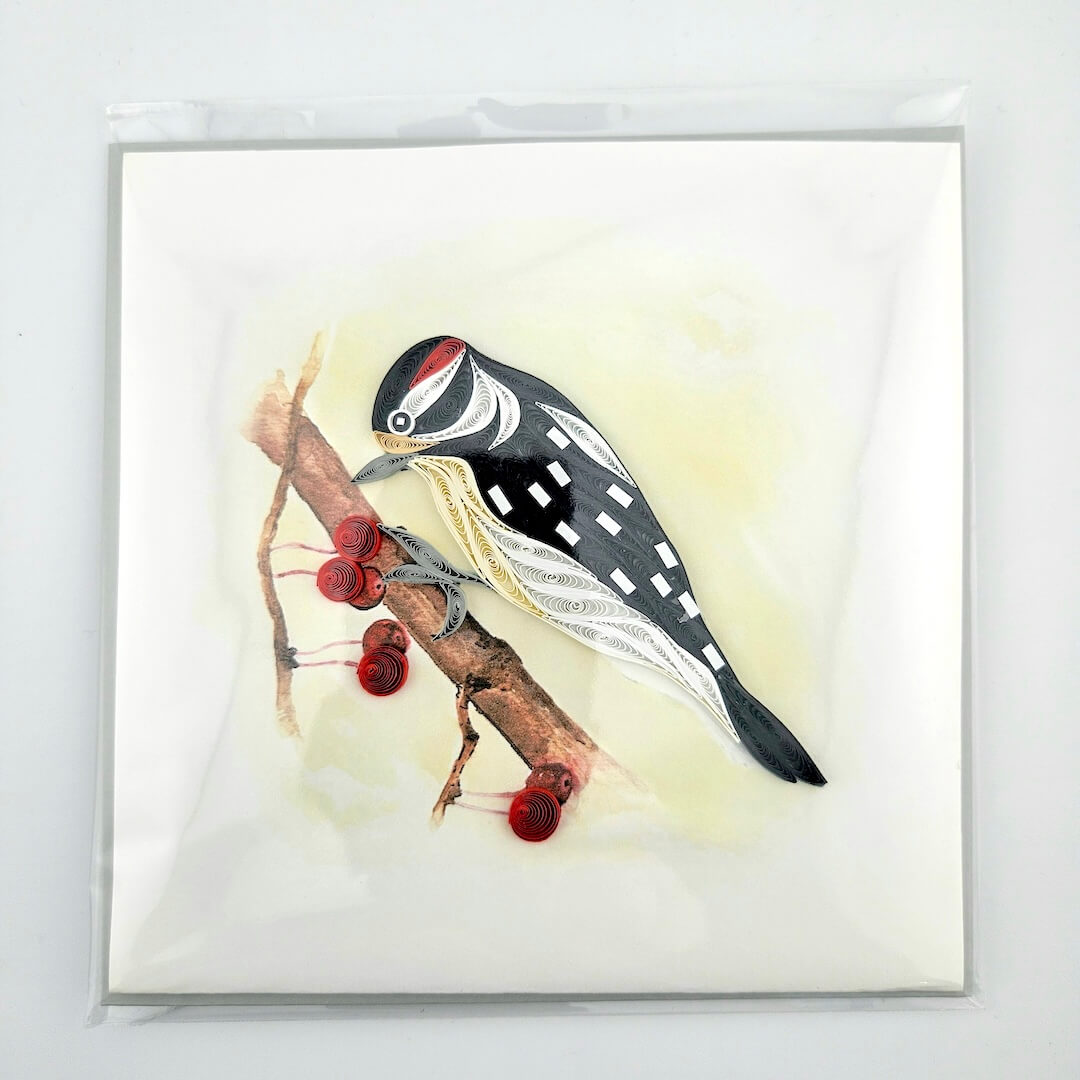 Quilled artwork of a bird perched on a branch with red berries against a light background