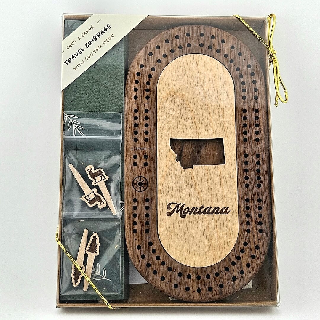 Wooden cribbage board with state silhouette in center above, "Montana" in curvy print, 2 sets of 2 pegs, trees & deer topped
