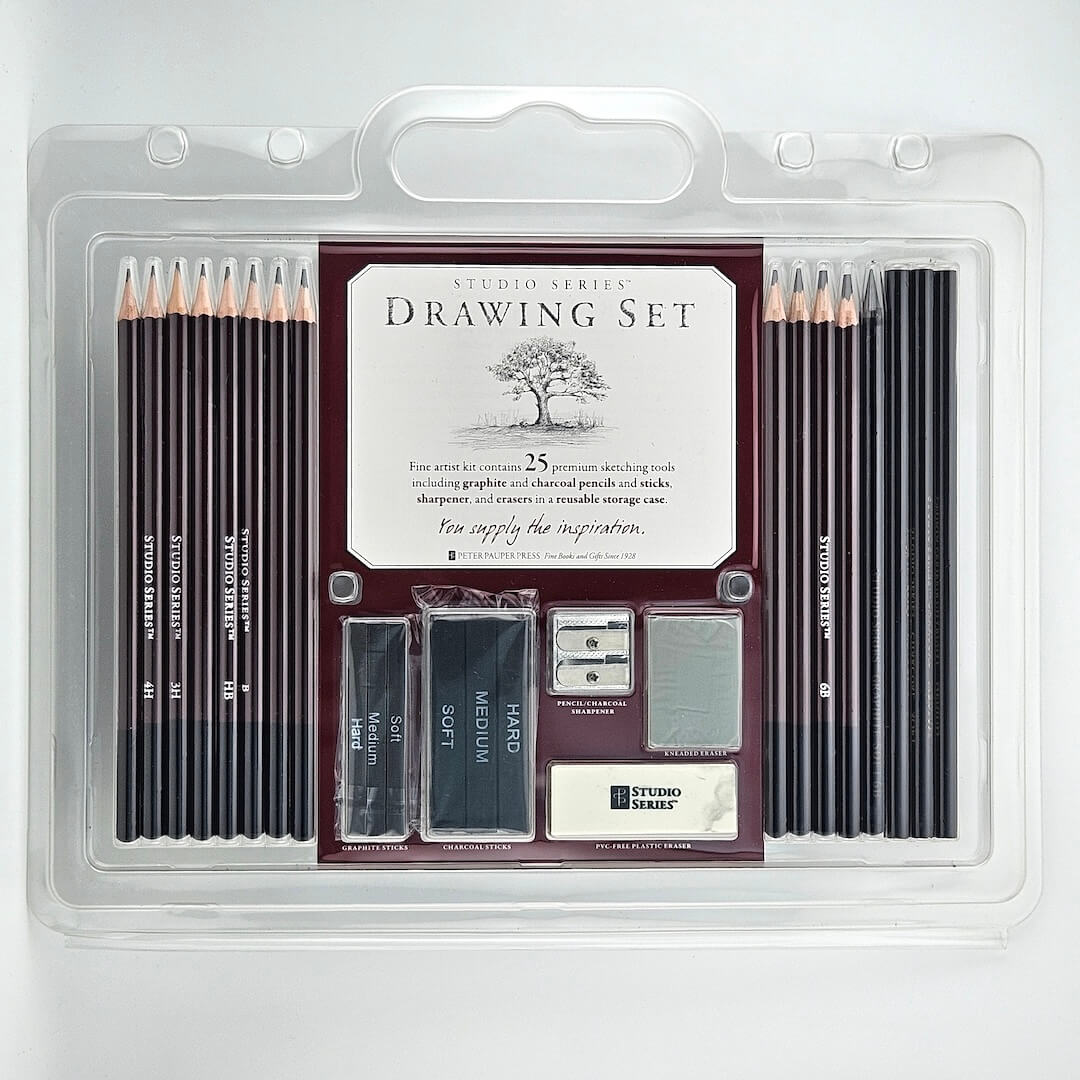 Drawing Set with pencils, charcoal, sharpeners and erasers in clear packaging against white background.