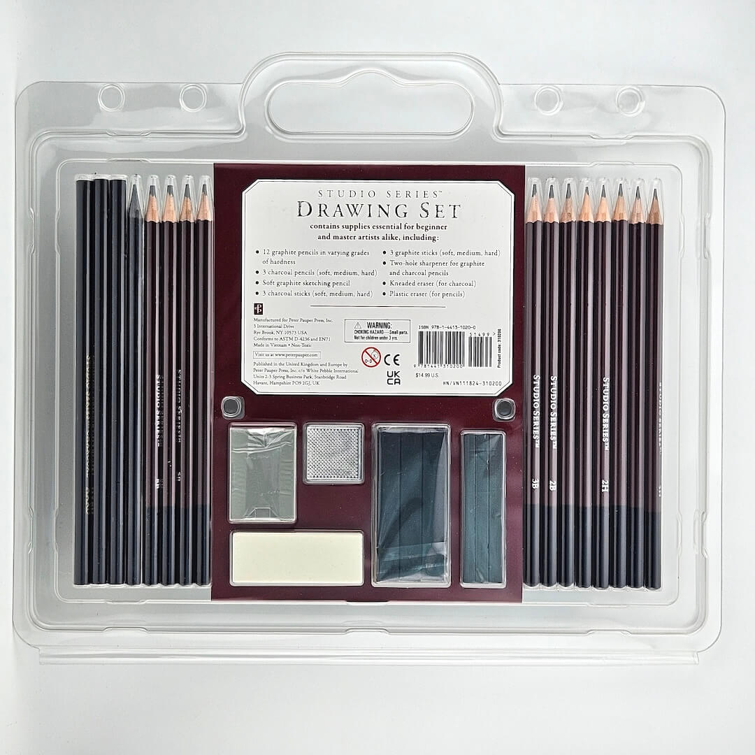 Drawing Set with pencils, charcoal, sharpeners and erasers in clear packaging against white background.