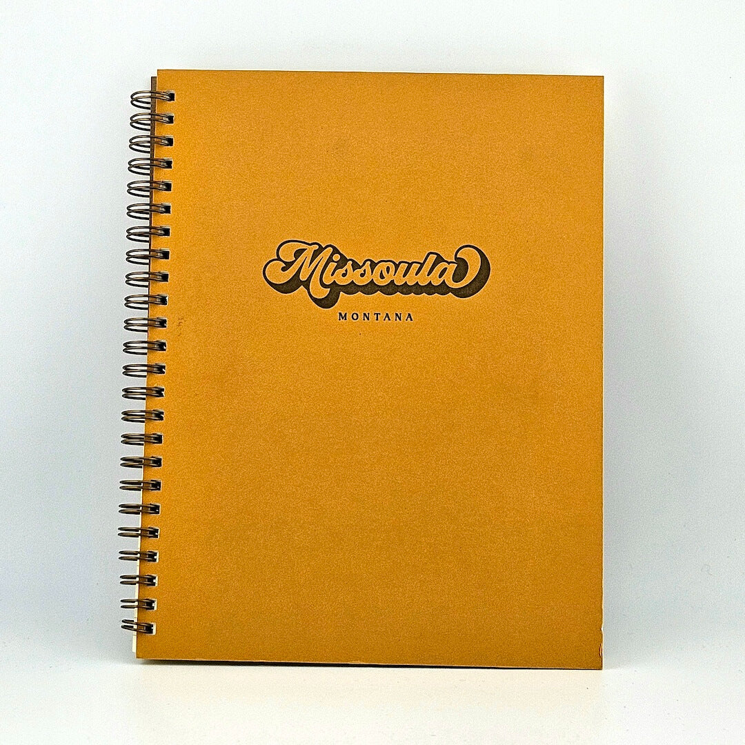 Mustard yellow, spiral-bound notebook against white background.