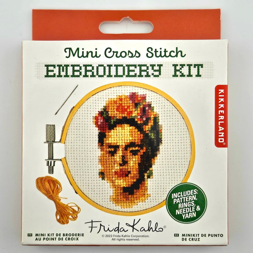 Mini cross stitch kit with pattern of Frida's face in orange and white packaging against white background.
