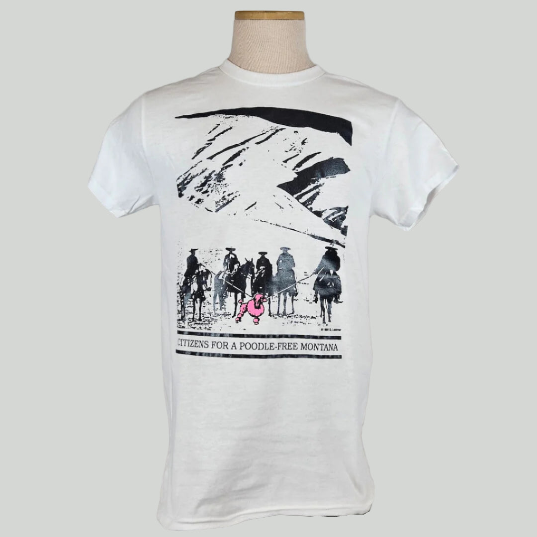 White shirt with mountain landscape behind group of mounted cowboys herding pink poodle with lassos. Caption under image.