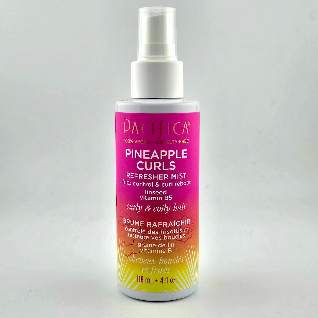 Pink/orange ombre spray bottle with white text with product information against white background.