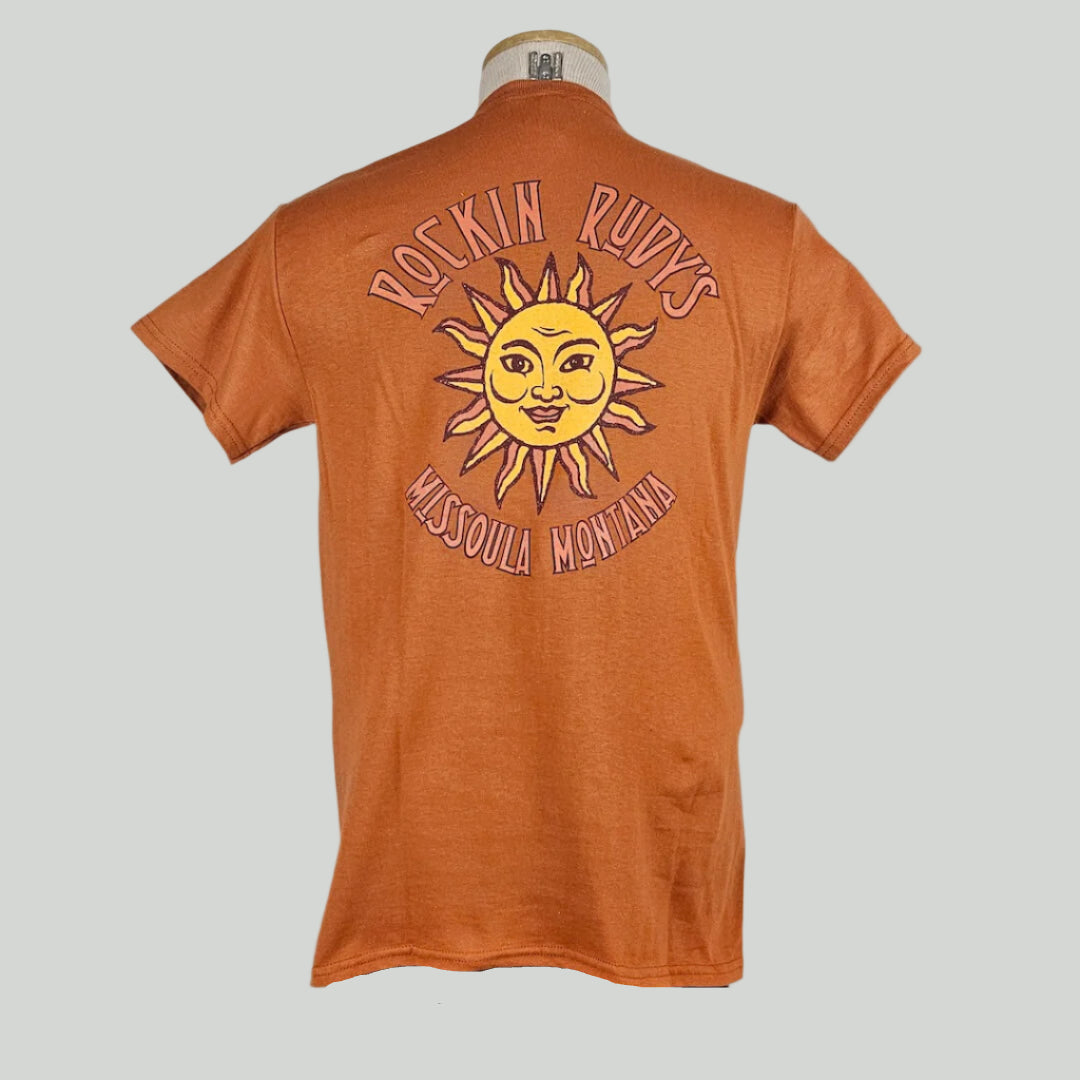 Orange colored t-shirt with large sun in center with "ROCKIN RUDY'S" & "MISSOULA, MONTANA" encircling it.