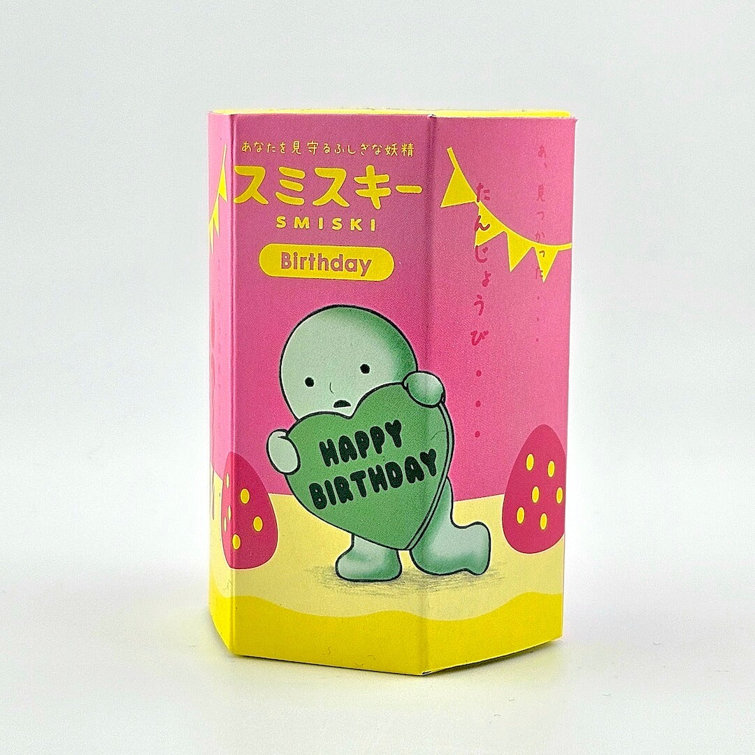 SMISKI birthday card with a green character holding a heart-shaped 'Happy Birthday' message on a pink and yellow background.