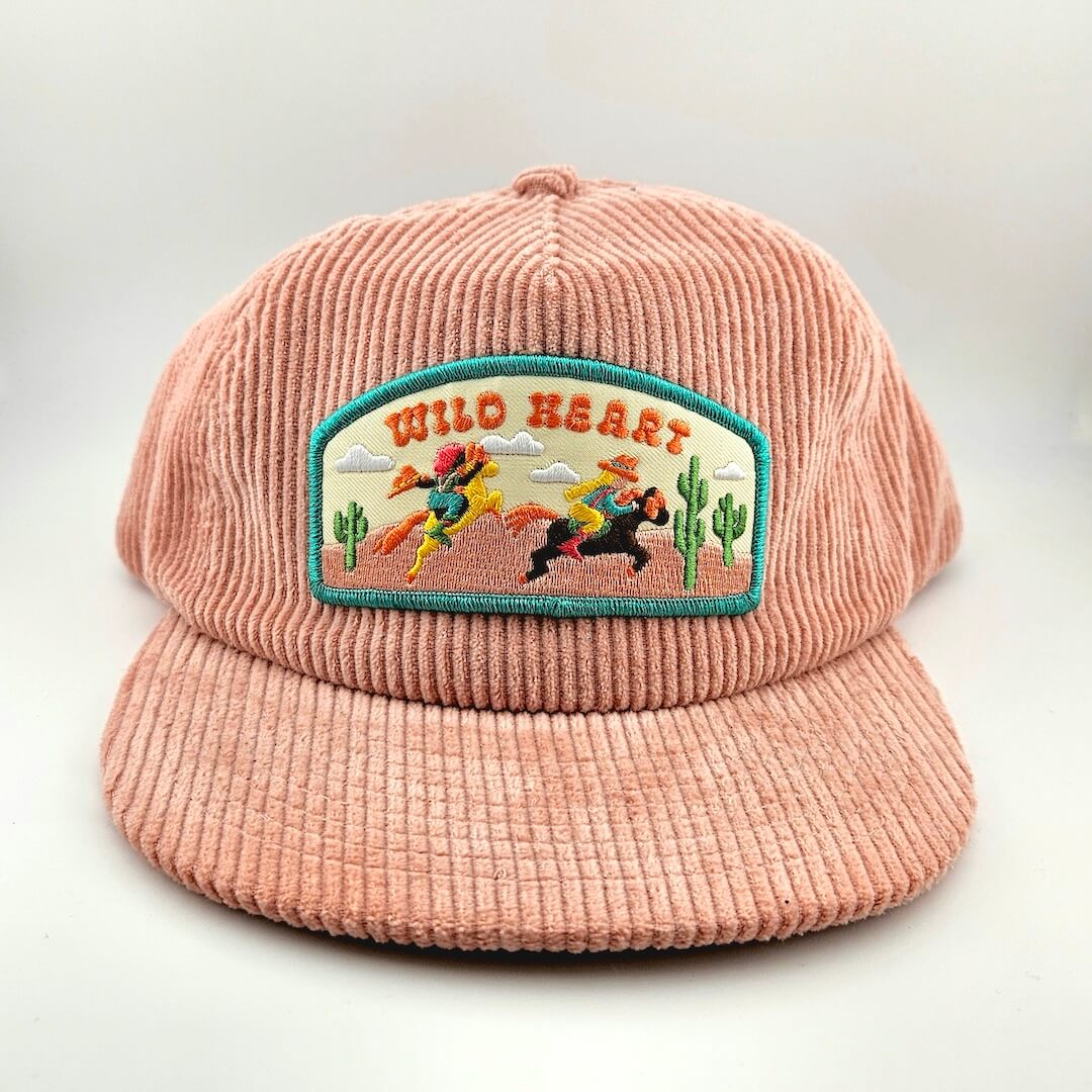 Pink corduroy cap with 'Wild Heart' patch featuring a cowboy and cacti design on a white background.