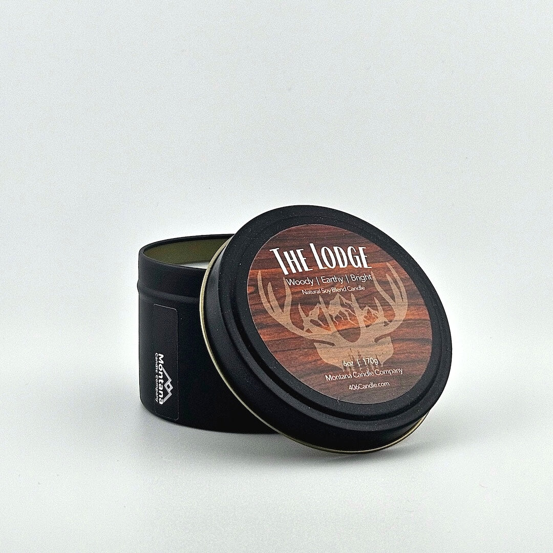 Black candle tin with scent name & listed scent components above deer horns on mountains, company at bottom.