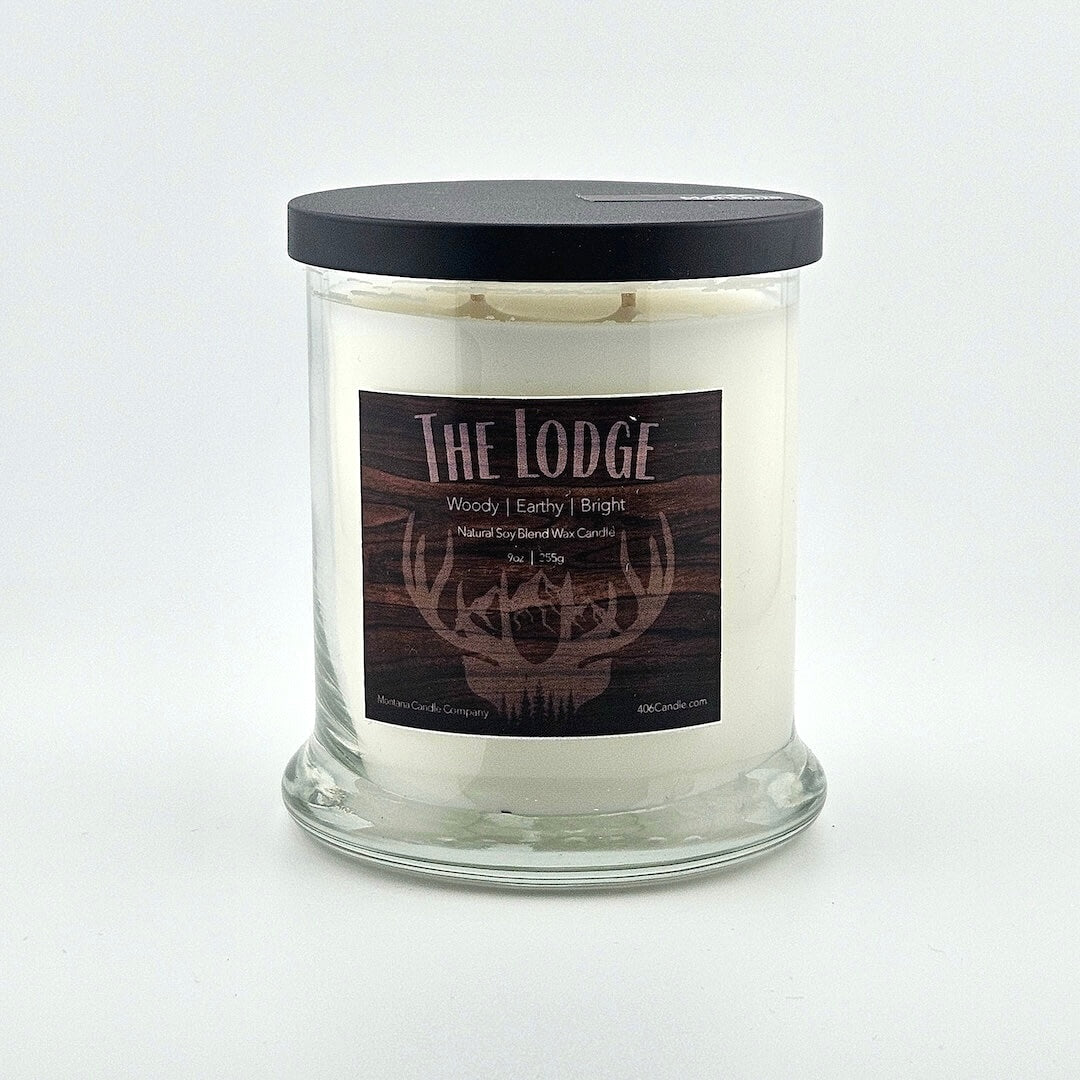 Glass jarred candle with black lid, label with wood grain background with deer horns under printed name above listed scent components.