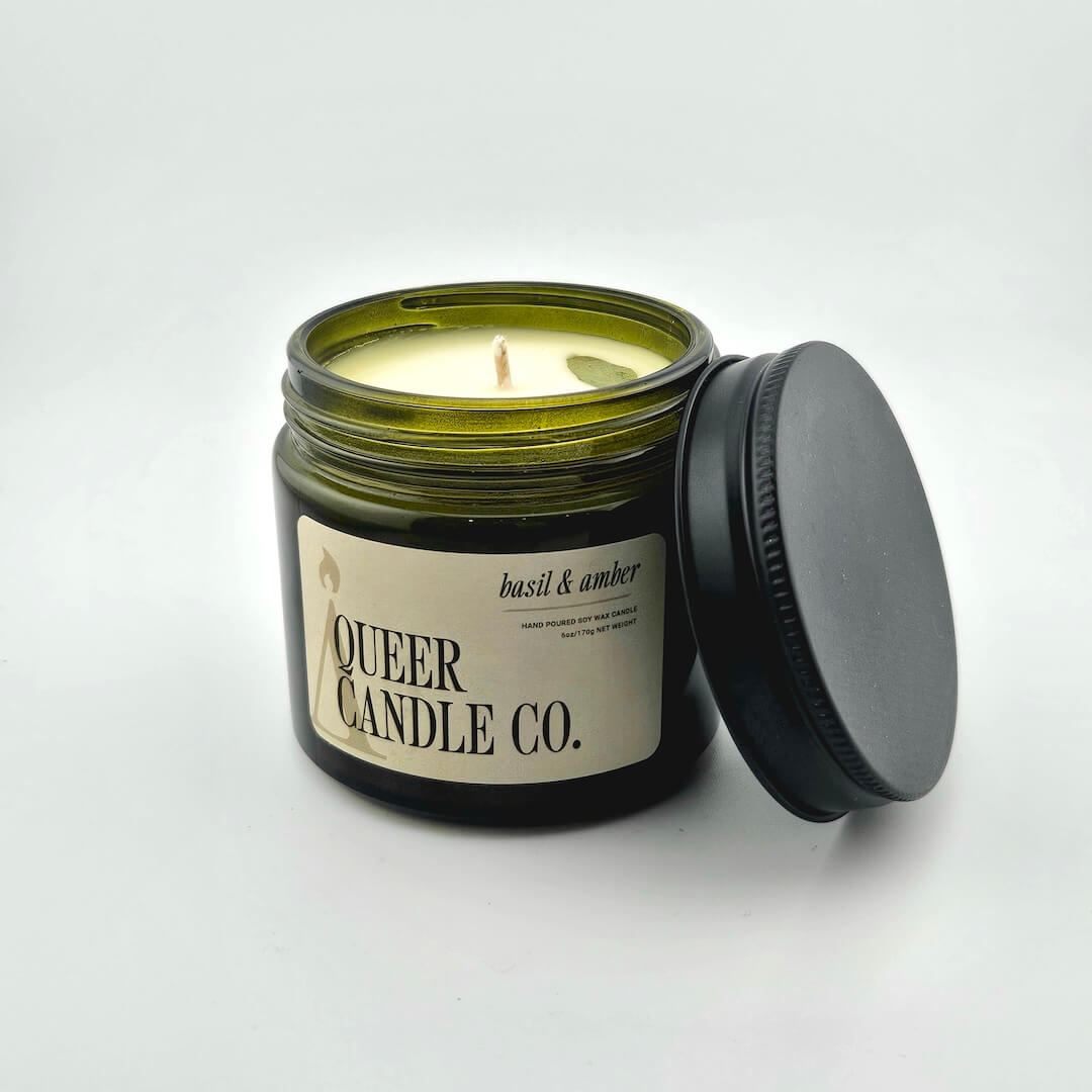 Green glass jar with black lid containing candle with label against white background.