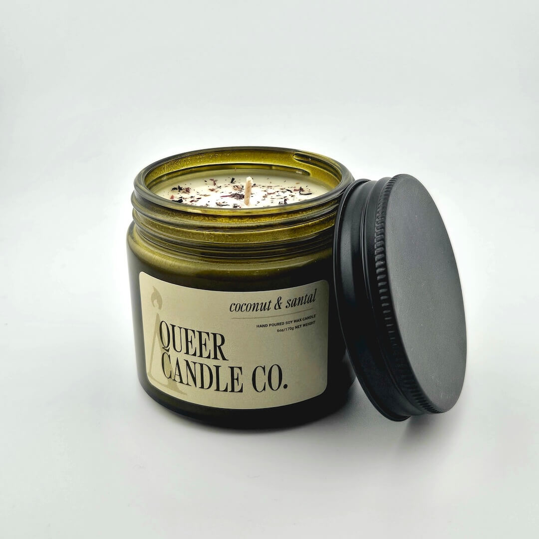 Green glass jar with black lid containing candle with label against white background.