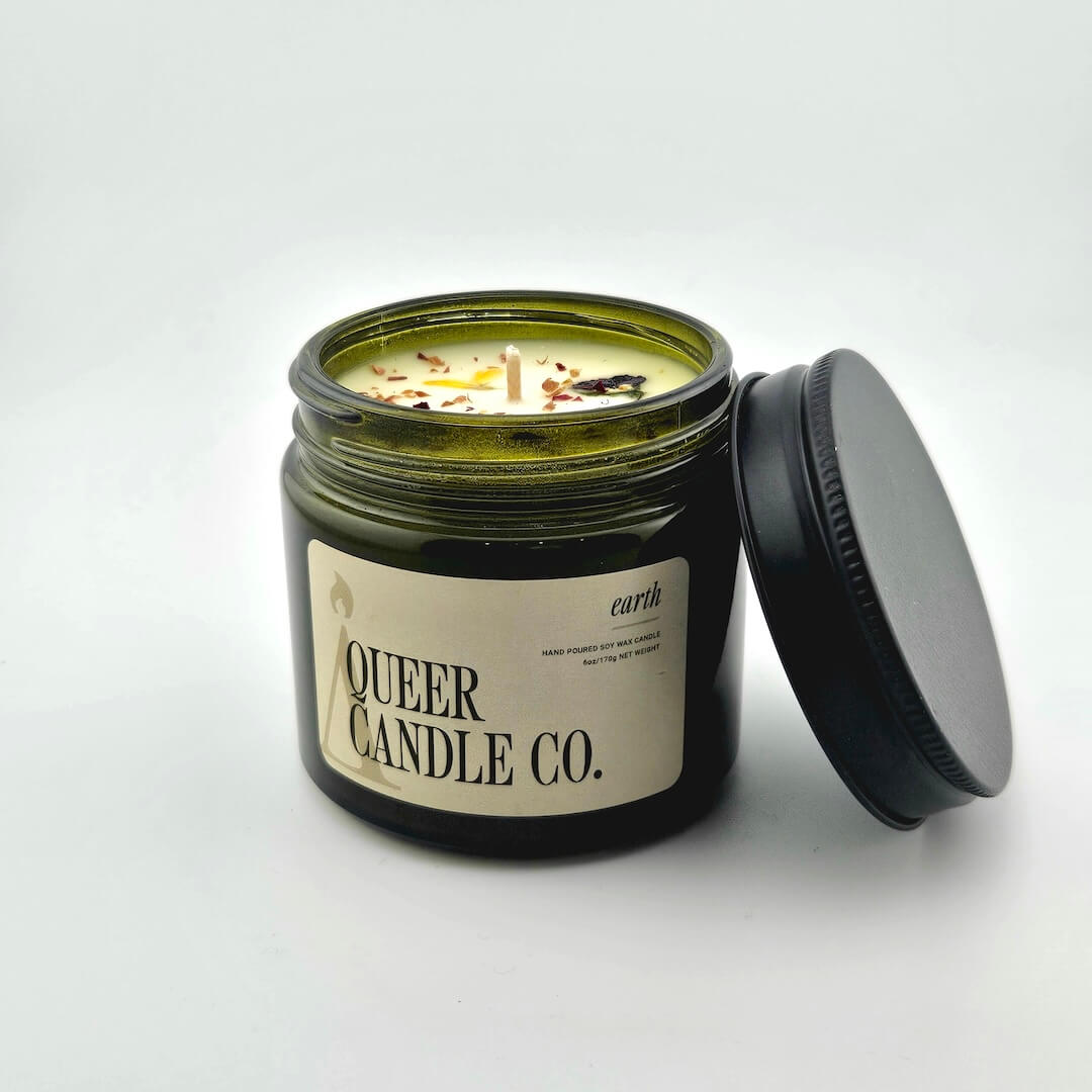 Green glass jar with black lid containing candle with label against white background.