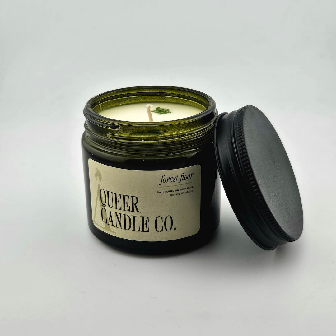 Green glass jar with black lid containing candle with label against white background.