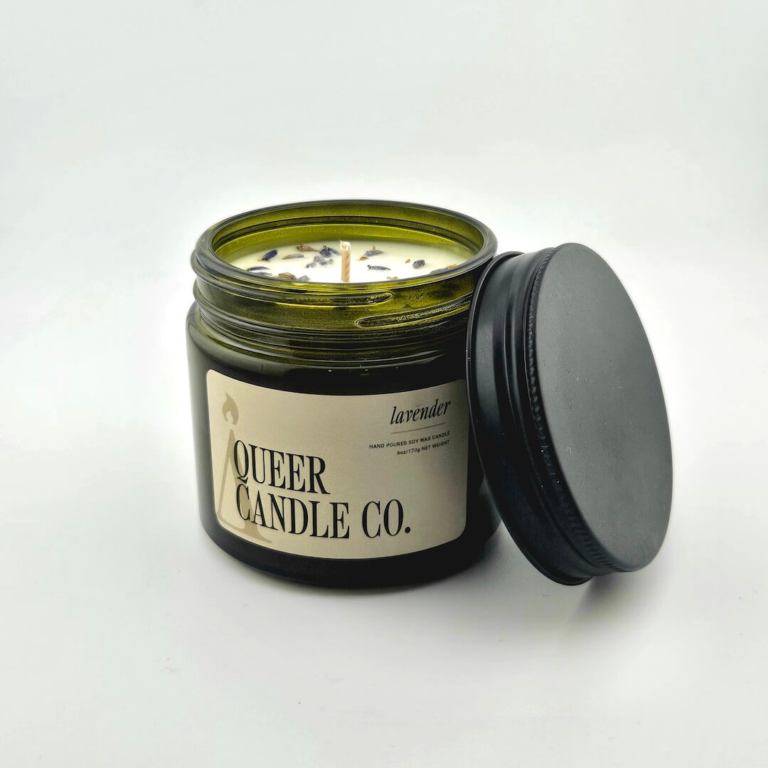 Green glass jar with black lid containing candle with label against white background.