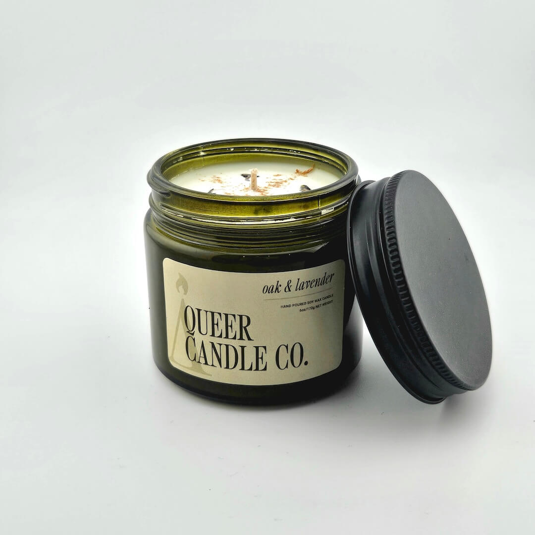 Green glass jar with black lid containing candle with label against white background.