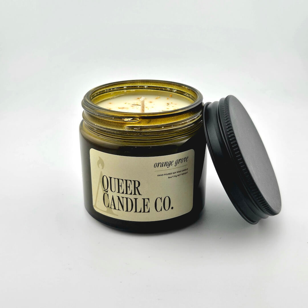 Green glass jar with black lid containing candle with label against white background.
