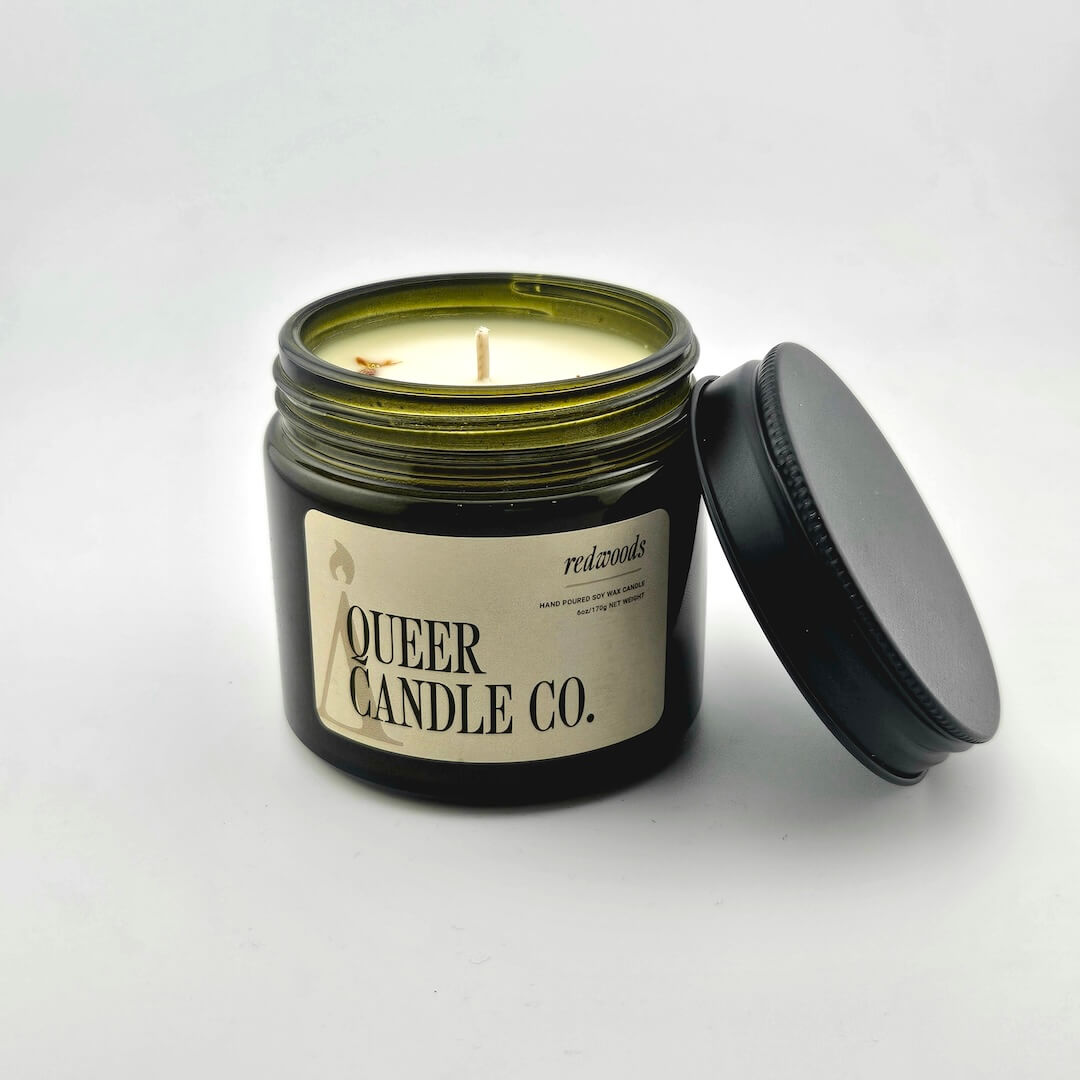 Green glass jar with black lid containing candle with label against white background.
