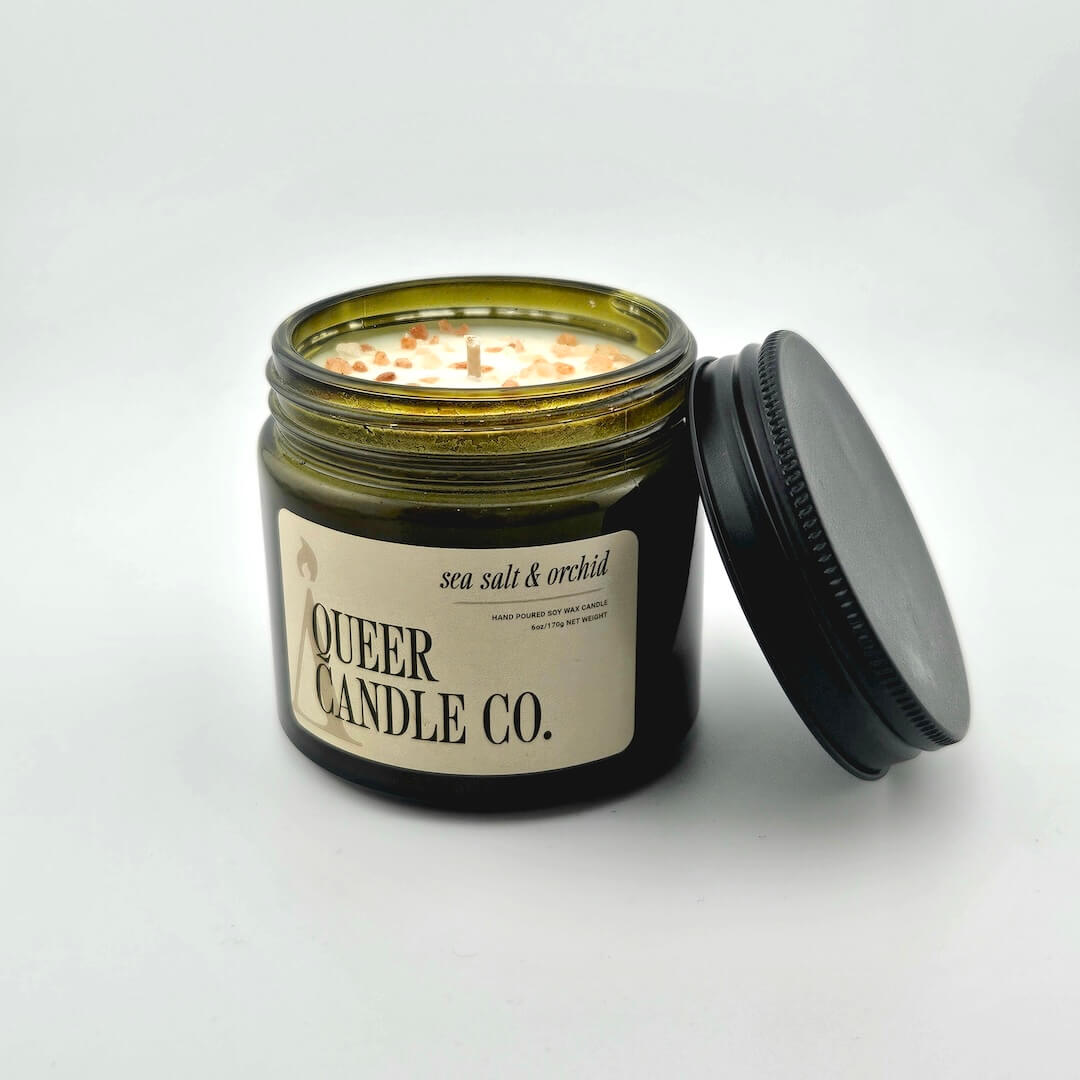 Green glass jar with black lid containing candle with label against white background.