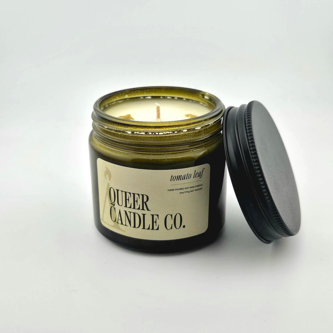 Green glass jar with black lid containing candle with label against white background.