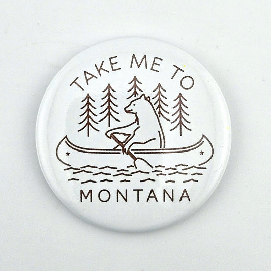 Button badge with bear in a canoe and text 'Take Me to Montana' on a white background
