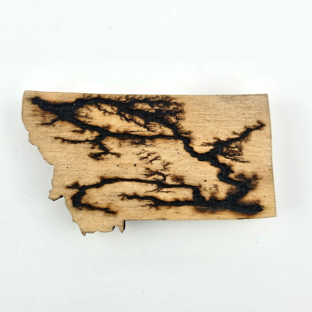 Wooden cutout of the state of Montana with burned designs on a white background