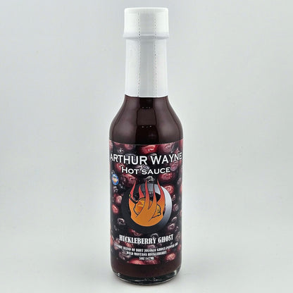 Glass bottle sealed with white plastic. Label has huckleberries pictured behind flaming pepper image in center. 