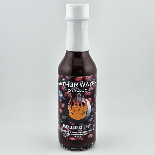 Glass bottle sealed with white plastic. Label has huckleberries pictured behind flaming pepper image in center. 