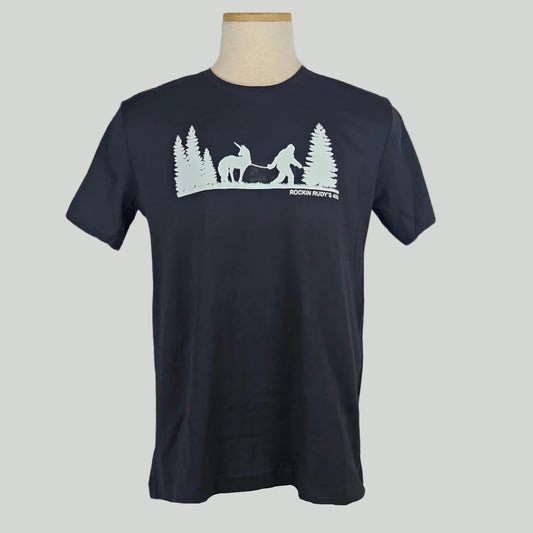 Black shirt with silhouette of trees either side of Bigfoot leading a unicorn on a leash in white print. 