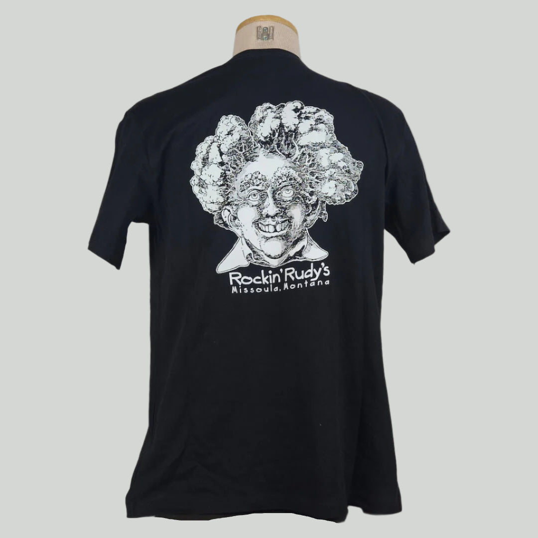 Black shirt with large smiling man’s head with trees for hair, "Rockin Rudy's, Missoula, Montana," printed below in center.