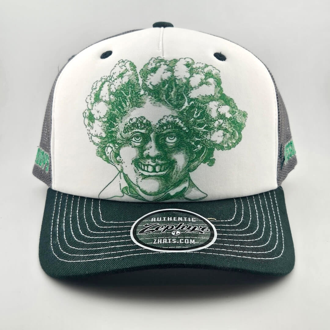 White face trucker hat with green mesh & bill featuring green stamp looking smiling man's head with trees for hair. 