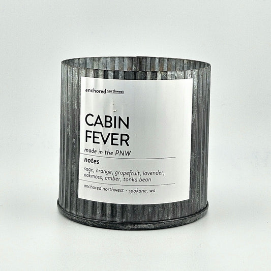 Candle labeled 'Cabin Fever' with a metal-textured container on a white background