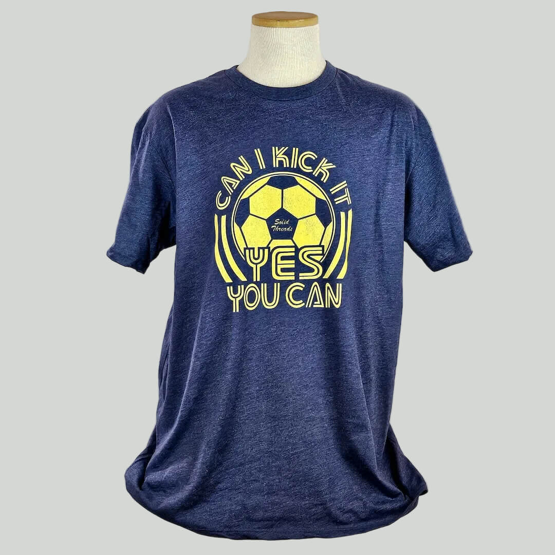 Blue t-shirt with yellow soccer graphic and text on a mannequin against a white background