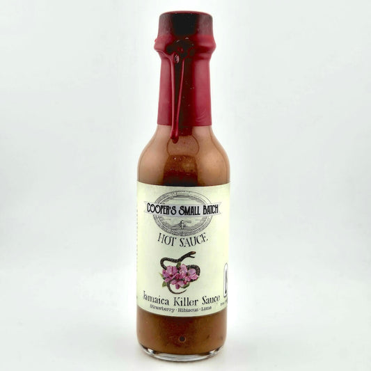 Bottle of Jamaica Killer Sauce with a red cap on a white background
