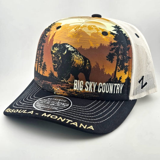 Trucker hat with mountain landscape across face with bison as central image. Missoula, Montana embroidered across bill. 