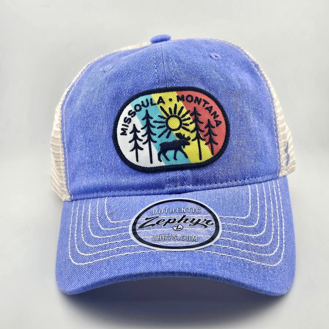Blue ball cap with white mesh back & stitching, multicolored patch on face with tree line drawing & city name.