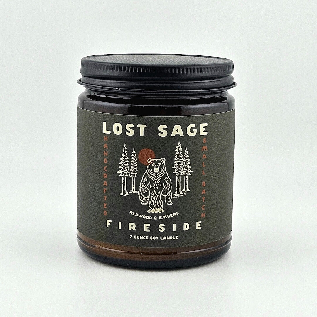 Candle jar labeled 'Lost Sage Fireside' with a bear and forest design on a white background