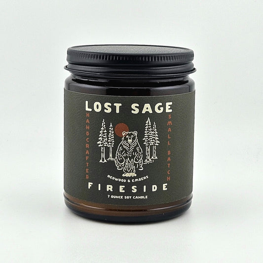 Candle jar labeled 'Lost Sage Fireside' with a bear and forest design on a white background